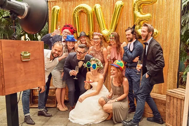 Glückliche Hochzeitsgäste posieren vor der Photobus Stand-Fotobox mit goldener LOVE-Deko. Top-Service für Fotobox mieten Schweiz.