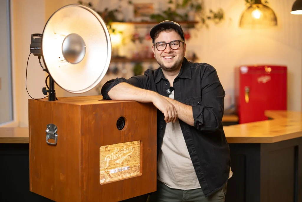 Lorenz Walter, Gründer von Photobus Schweiz, lehnt an einer Holz-Fotobox mit professionellem Studioblitz und Beauty Dish.