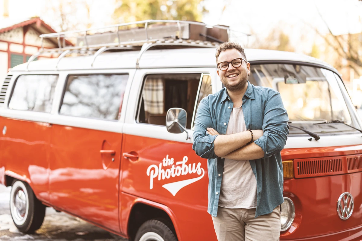 Lorenz Walter steht vor dem roten Photobus und lächelt in die Kamera, Gründer von Photobus Schweiz.