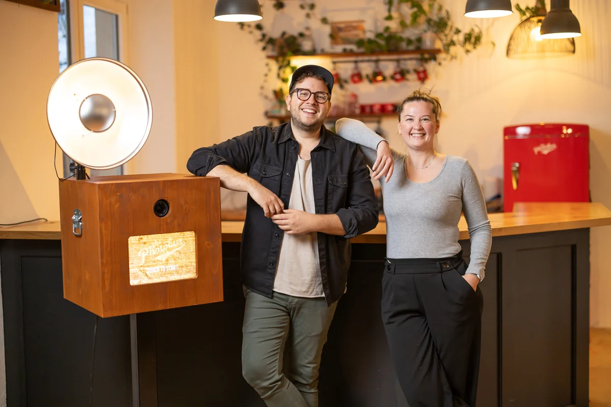 Das Kern-Team von Photobus Schweiz lächelt neben einer hölzernen Fotobox in ihrer Zentrale (Photobus Studio in Wetzikon Zürich) – Symbole für Erfahrung aus 8'000 Vermietungen und 1'000 Events jährlich.