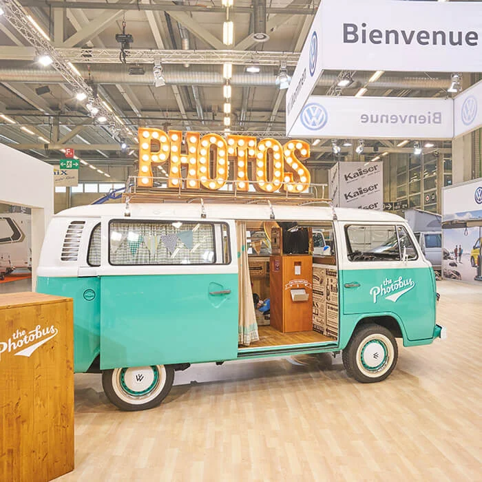 Türkiser Photobus VW-Bus mit PHOTOS-Schild aufgebaut an einem Messestand in der Schweiz