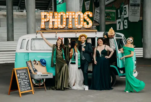 Brautpaar mit Trauzeugen vor dem grünen Photobus mit leuchtendem PHOTOS-Schild beim FC St. Gallen Kybunpark