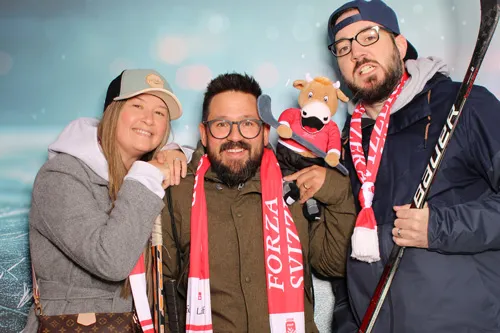 Drei begeisterte Schweizer Eishockey-Fans posieren an der Photobus Fotobox an der IIHF WM 2026 mit Hockeyschlägern, Forza-Svizzera-Schals und WM-Maskottchen
