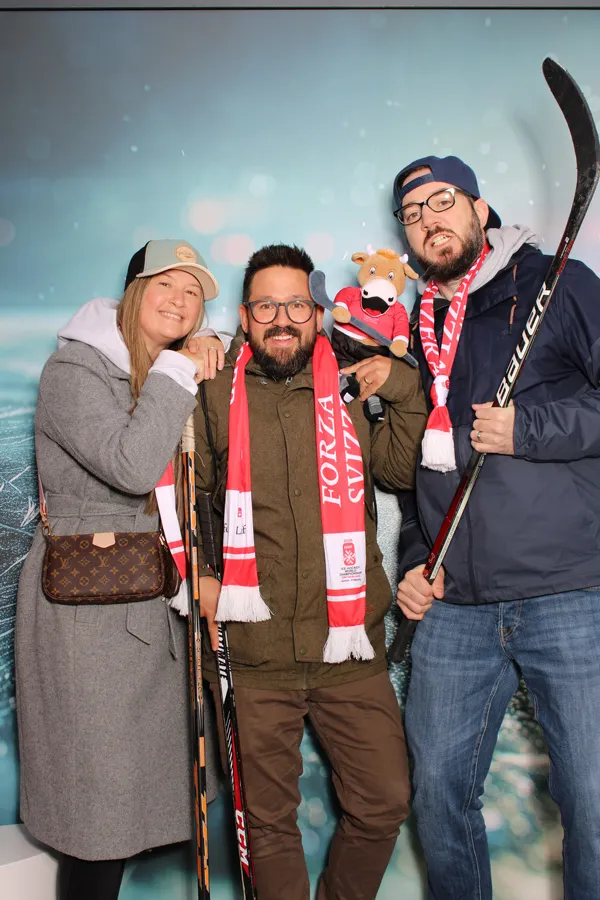 Drei begeisterte Schweizer Eishockey-Fans posieren an der Photobus Fotobox an der IIHF WM 2026 mit Hockeyschlägern, Forza-Svizzera-Schals und WM-Maskottchen