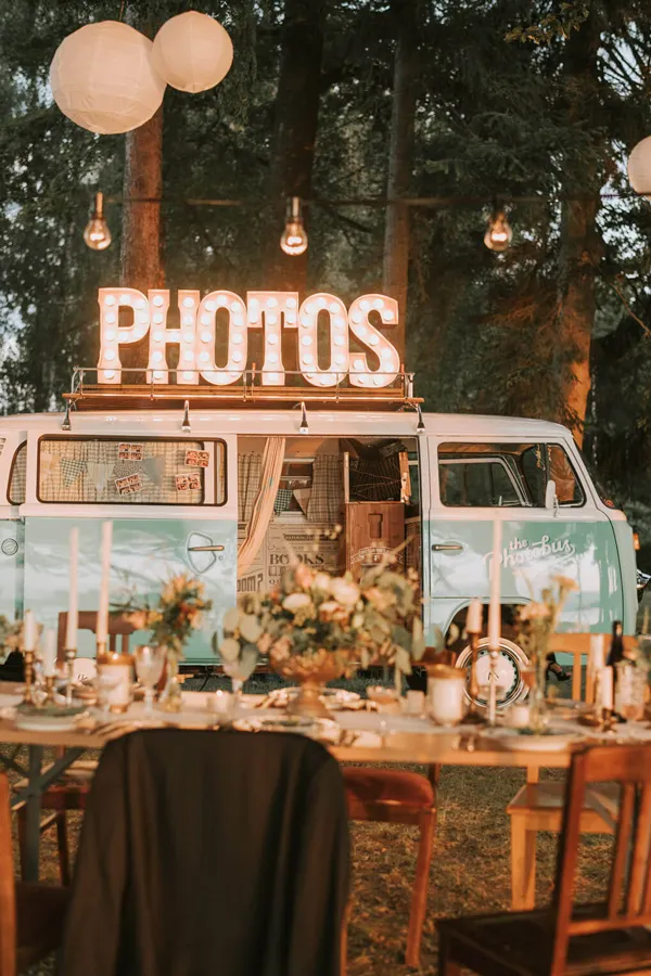 Photobus mit leuchtendem PHOTOS Schild und gedecktem Hochzeitstisch mit Lichterketten