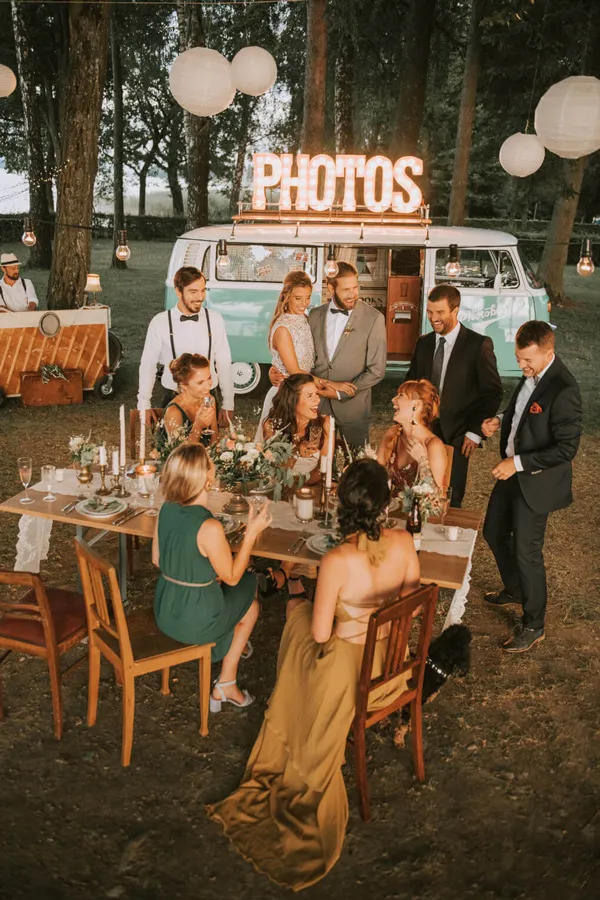 Photobus Fotobox bei Hochzeit im Wald mit Gästen an gedecktem Tisch und Lichterkette