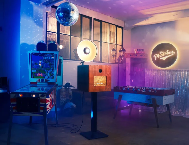 Photobus Holzfotobox im blauen und violetten Partylicht mit Discokugel, Flipper und Töggelikasten im Hintergrund