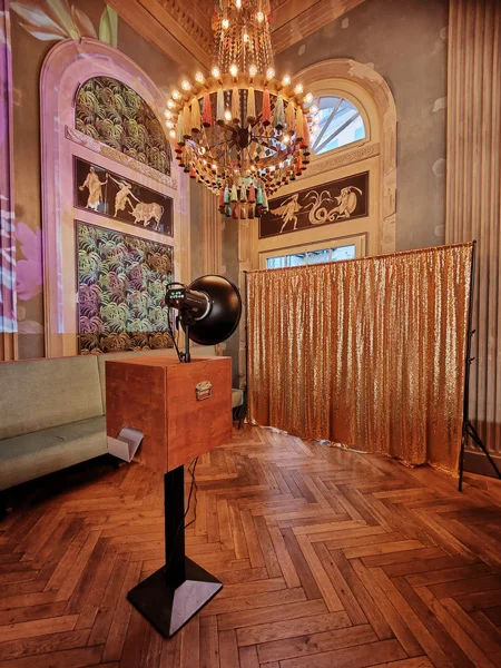 Photobus Fotobox vor goldenem Glitzervorhang in einem historischen Saal mit Kronleuchter und Parkettboden