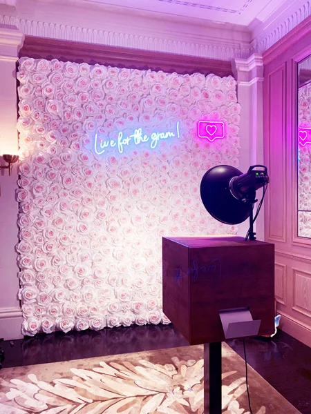 Photobus Holzfotobox vor einer weissen Rosenwand mit pinkem Neon-Schriftzug Live for the gram bei einem eleganten Event