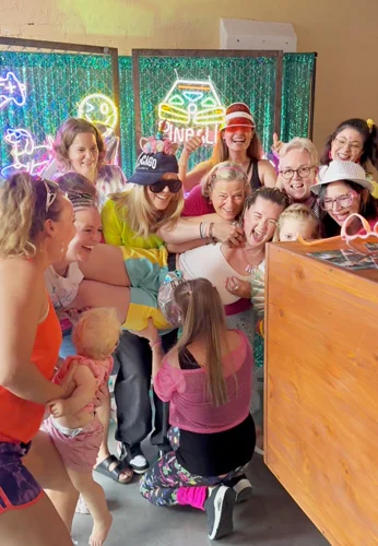Gruppe von Gästen lacht und feiert gemeinsam an der Photobus Fotobox aus Holz mit buntem Neon-Hintergrund